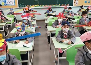 Povinné odstupy ve školách jako ochrana před koronavirem: Školáci v čínském Chang-čou nosí speciální čepice s metrovými tyčemi