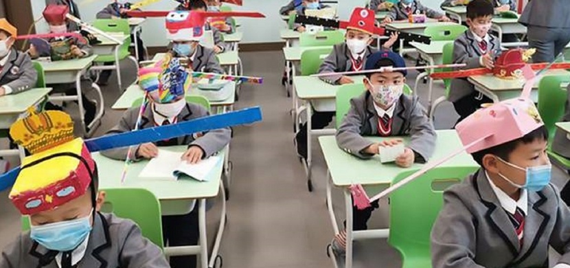 Povinné odstupy ve školách jako ochrana před koronavirem: Školáci v čínském Chang-čou nosí speciální čepice s metrovými tyčemi